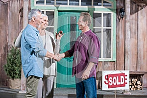 Wife holding keys of new house while her husband shaking hands with saleman photo