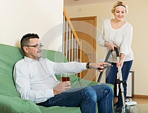 Wife hoovering room, husband relaxing