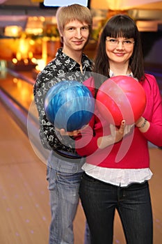 Wife and husband with balls stand in bowling club