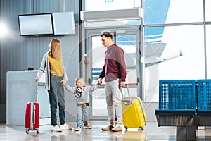 Wife and husband holding hands with daughter and standing neat suitcases