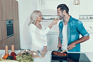 The wife makes salad, while husband fries meat in kitchen.