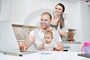 Wife massaging shoulders of husband with baby before laptop