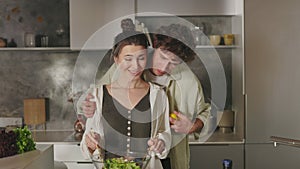 Wife mixing salad while husband kissing and hugging her