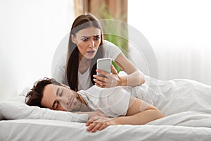 Wife Reading Husband& x27;s Messages On Smartphone While He Sleeping Indoor