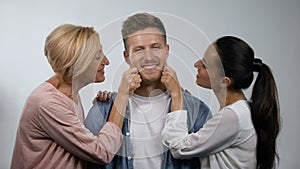 Wife and senior mother pinching young man cheeks, overprotection in family