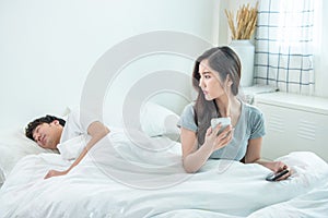 Wife spying the phone of her husband while man sleeping in bed at home.asian young girl check and suspension on boyfriend phone