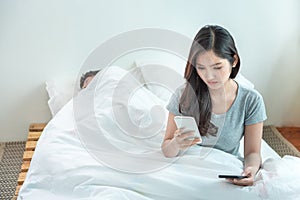 Wife spying the phone of her husband while man sleeping in bed at home.asian young girl check and suspension on boyfriend phone