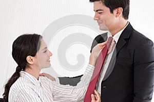 Wife tying red necktie to her husband in the office with smiling and happy