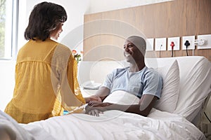 Wife Visiting And Talking With Patient Husband In Hospital Bed