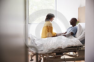 Wife Visiting And Talking With Patient Husband In Hospital Bed