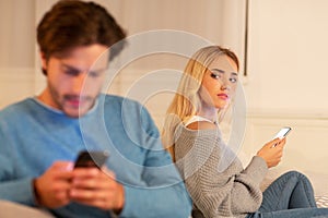 Wife Watching Husband Texting On Phone Suspecting Infidelity Sitting Indoor