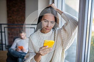 Wife wearing beige sweater feeling confused reading message