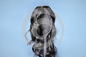Wig, alopecia and chignon. Comb with black wig on a blue background, similar to woman's head. Concept of hair care photo