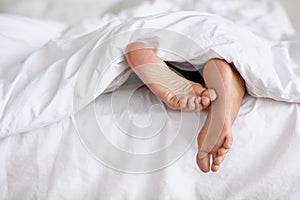 Wiggling toes of wakefulness. a pair of womans feet poking out from under the sheets of a bed.