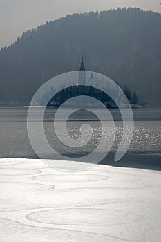 Wiinter view of frozen Bled lake with ice and snow at sunrise, sunny winter morning in Slovenian mountains