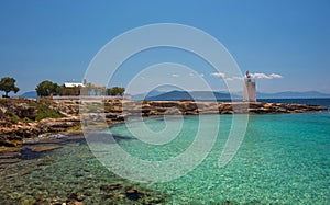 The wild coast of Aegina island with clear and blue waters of Mediterranean sea and the old small lighthouse in the background, in