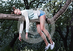 Wild fatigue. Beautiful young woman sleeping on a tree branch. Feet and hands hanging down