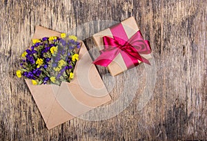 Wild flowers in an envelope and a gift box with a bow on an old wooden background. Romantic concept.