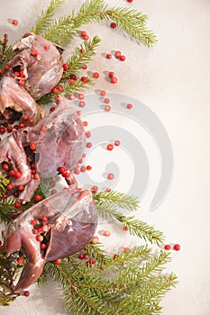 Wild hunting fowls in cooking. Ptarmigan, fir-tree branches and cowberry arranged on light background.