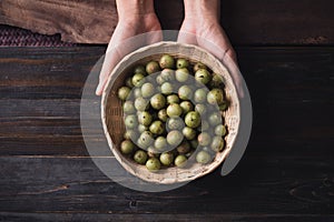 Wild Indian gooseberry or amla in a bamboo basket holding by hand