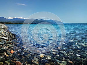 Wild pebble beach view with blue sky and mountains