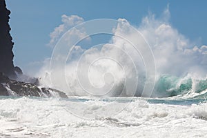 Wild, powerful wave splashing, crashing on rocky shore, under bl