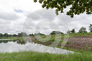 Wild river and green grass in summer cloudy landscape.