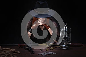 wild west girl with revolver gun sitting at the table with ammunition and silver coins