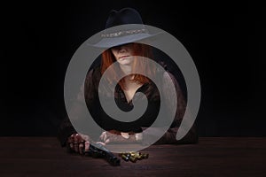 wild west girl with revolver gun sitting at the table with ammunition and silver coins