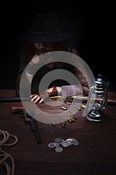 wild west girl with revolver gun sitting at the table with ammunition and silver coins