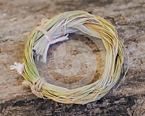 Wildcrafted dried Sweetgrass Hierochloe odorata wrapped in organic cotton string. On tree bark in forest. Smudging ritu