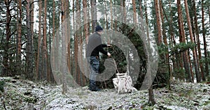 Wilderness survival camp - man building tree branch hut in forest in winter