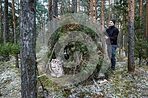 Wilderness survival camp - man building tree branch hut in forest in winter