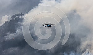 Wildfire Service Helicopter flying over BC Forest Fire and Smoke on the mountain near Hope