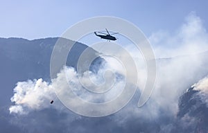 Wildfire Service Helicopter flying over BC Forest Fire and Smoke on the mountain near Hope