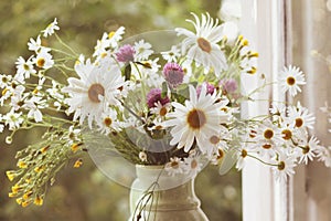 Wildflowers along with daisies in ceramic vase in vintage styl.