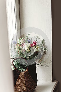 wildflowers in wicker bag on rustic white window. colorful flowers in brown basket in sunlight, space for text. rural atmospheric