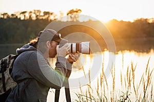 Wildlife photographer with camera photographing nature on lake at sunset