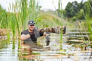 Wildlife photographer outdoor, standing in the water. Wildlife photographer in summer time working in the wild. Wildlife