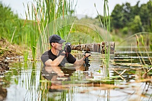 Wildlife photographer outdoor, standing in the water. Wildlife photographer in summer time working in the wild. Wildlife