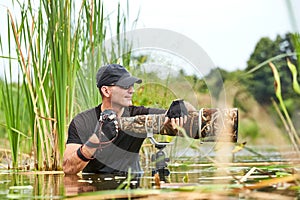 Wildlife photographer outdoor, standing in the water. Wildlife photographer in summer time working in the wild. Wildlife