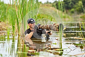 Wildlife photographer outdoor, standing in the water. Wildlife photographer in summer time working in the wild. Wildlife