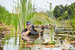 Wildlife photographer outdoor, standing in the water. Wildlife photographer in summer time working in the wild. Wildlife