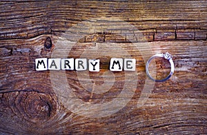 Will you marry me? An offer of marriage on rustic background. Wording `Marry me` written with little cubes and wedding ring near