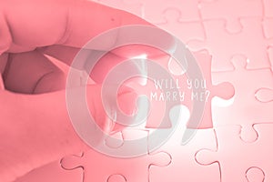 Will you marry me word on pink jigsaw puzzle being holding by th