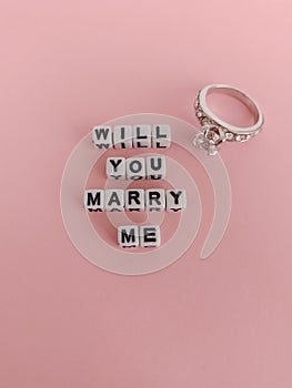 Will you marry me words on a light pink background and a beautiful silver diamond engagement ring