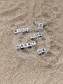 Will you marry me words written on sand at the beach with a beautiful engagement ring