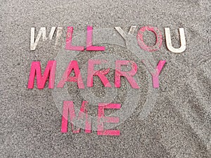 Will you marry me written on sand and partially covered by sand