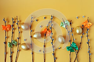 Willow branches, colorful bows made of satin ribbons, golden eggs on a yellow background, top view, space for text