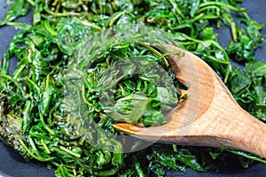 Wilted arugula or rocket salad, preparing a side dish in frying pan, horizontal closeup